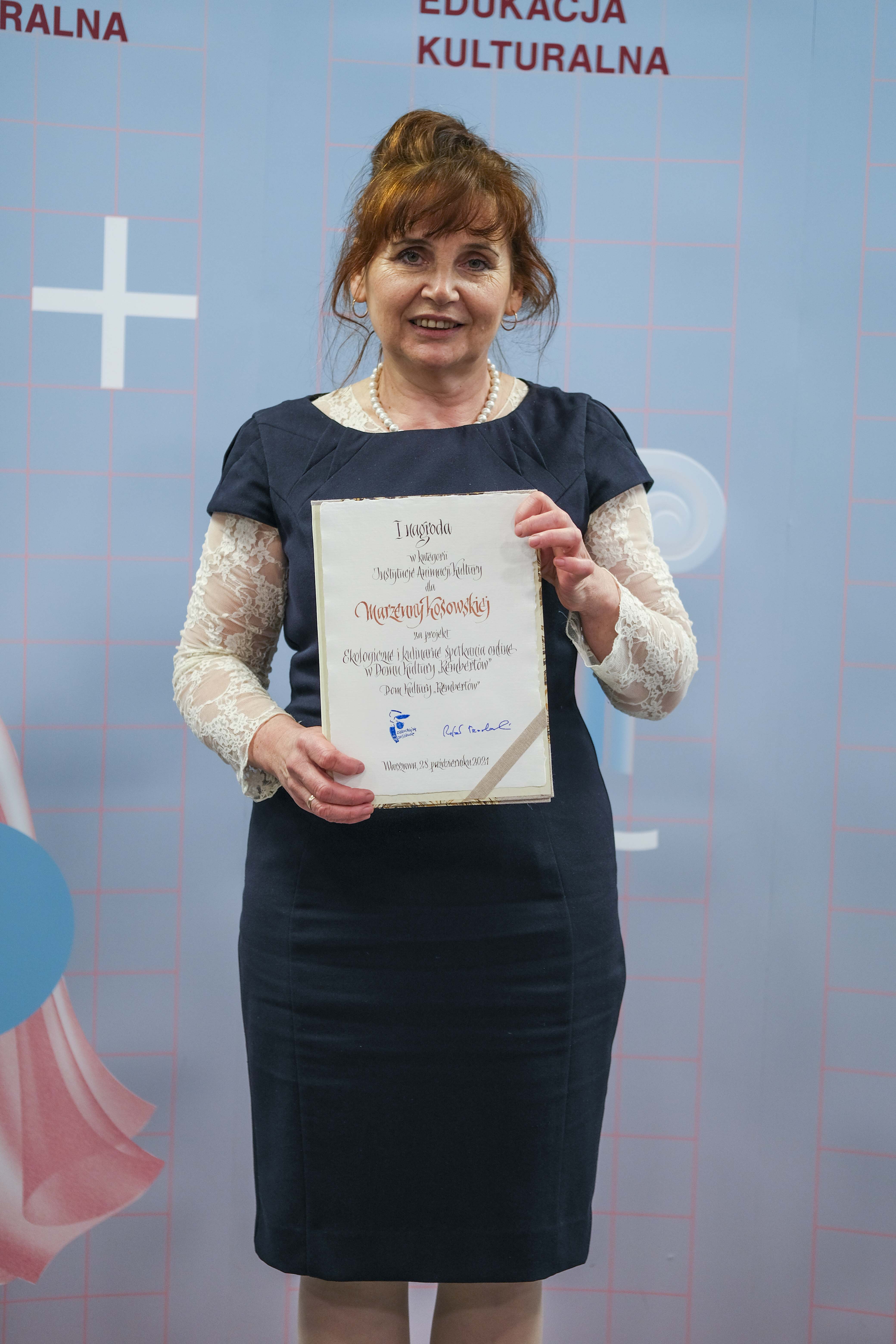 Na tle ścianki prasowej pozuje z dyplomem Marzenna Kosowska, laureatka 1 miejsca Warszawskiej Nagrody Edukacji Kulturalnej 2021, w kategorii instytucje kultury.