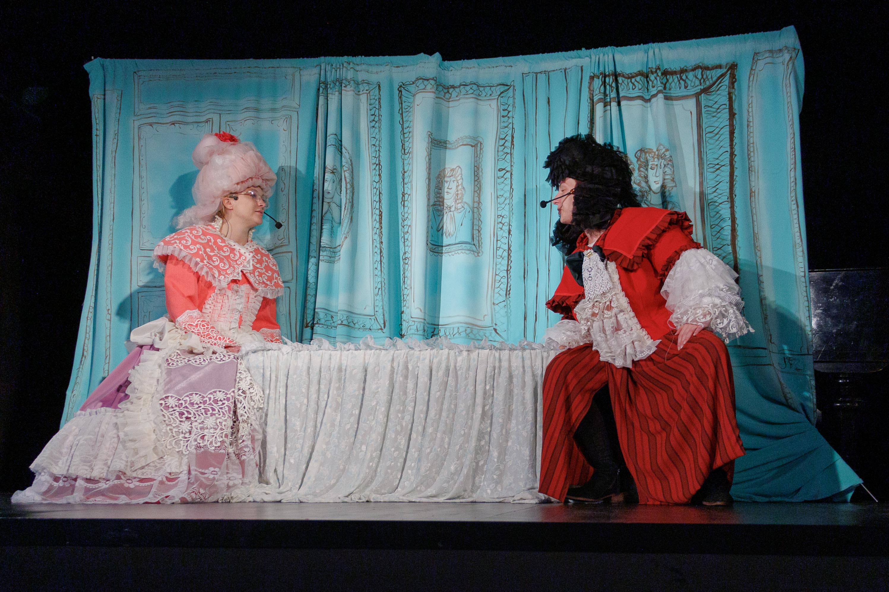 Na scenie widać dwie osoby, ubrane w ozdobne, barokowe stroje i peruki